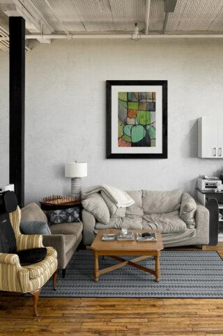 Kubistyczny, abstrakcyjny obraz w odcieniach zieleni wisi nad kanapą w salonie.